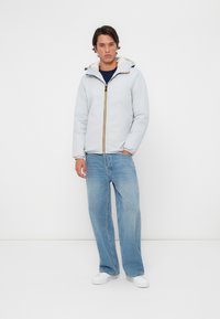 Lys grå isolert jakke med hette, har en kontrasterende gul glidelås, kombinert med løs passform blå denim jeans og hvite sko.