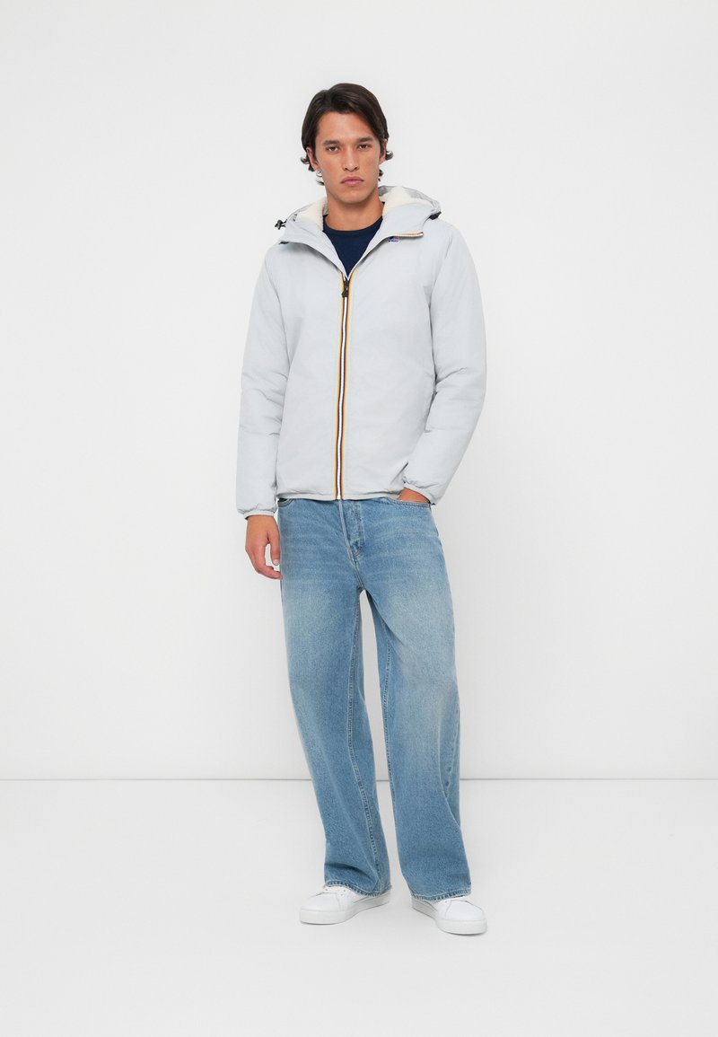 Lys grå isolert jakke med hette, har en kontrasterende gul glidelås, kombinert med løs passform blå denim jeans og hvite sko.