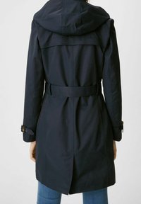 Trench-coat bleu marine avec capuche, taille ceinturée et détails de boutons aux poignets. Présente des lignes épurées et un design structuré à l'arrière.