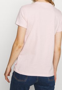 Camiseta de algodón de color rosa claro con mangas cortas, escote redondo y una pequeña etiqueta con el logo en la costura lateral. Textura suave, corte casual.