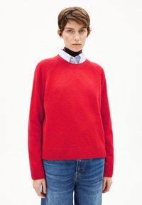 Rode gebreide trui met een ronde hals, raglanmouwen en ribgebreide zoom. Gecombineerd met een blauwe overhemd met kraag en denim broek.