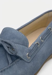 Μπλε καστόρινο παπούτσι με λεπτομέρεια φιόγκου, μεταλλικά ιριδίσματα και αντιθετική ραφή. Μαλακή υφή με στρογγυλεμένη μύτη και επίπεδη σόλα.