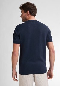 Námořnický pletený svetr s krátkým rukávem a kulatým výstřihem, s žebrovanými manžetami a spodním lemem, hladkou texturou a minimalistickým designem.