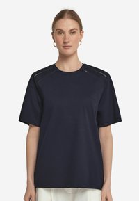 Mörkblå kortärmad t-shirt i mjukt tyg, med utskärningar på axelsömmarna, avslappnad passform och rundad halsringning.