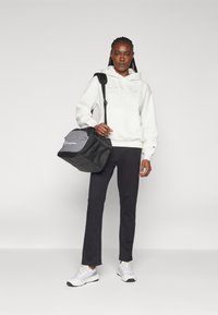 Sudadera blanca con capucha, pantalones negros y bolso de deporte gris/negro. Zapatillas blancas con detalles grises. Ropa atlética simple y casual.