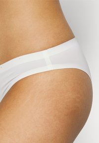 Fehér fehérnemű sima, rugalmas derékrésszel és minimalista dizájnnal. Az anyag enyhén áttetsző, lágy tapintású.