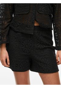 Czarny komplet szydełkowy zawierający wzorzystą kurtkę o przezroczystej teksturze oraz dopasowane szorty. Oba elementy mają kwiatowe wzory i luźny krój.