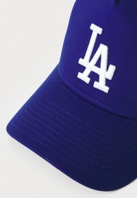 Lilla baseballcap med en struktureret design, der har et hvidt broderet "LA"-logo på fronten og tekstilt stof på skyggen.