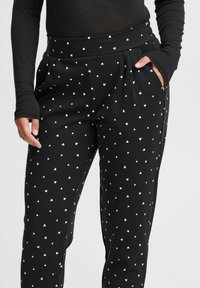 Zwarte broek met kleine witte hartpatronen, elastische tailleband en zijzakken. Gemaakt van een zacht, rekbaar materiaal.
