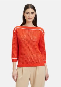Roter gestrickter Pullover mit einem lockeren, offenen Strickdesign, das weiße Streifenakzente am Halsausschnitt und an den Ärmeln aufweist. Dreiviertellange Ärmel.