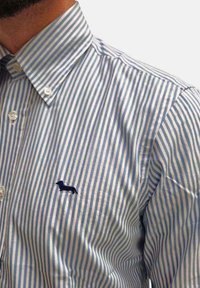 Camicia a righe blu e bianche con ricamo di un piccolo bassotto navy sul lato sinistro del petto e colletto classico. Tessuto in cotone.