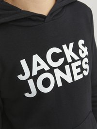 Črna kapuca z velikim belim grafičnim besedilom "JACK & JONES" natančno prikazanim na prsih. Mehka tkanina s kapuco.