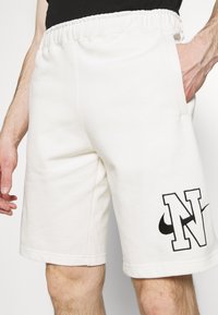 Vita shorts i bomullsblandning med elastisk midja, sidfickor och en kontrasterande svart "N" samt Nike-logotyp på vänster ben.
