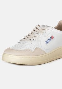 Sneaker bianca in pelle con accenti in suede beige, punta perforata, lacci piatti e marchio visibile di lato. Suola in gomma.