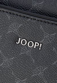 Zwart textiel materiaal met een subtiel patroon. Zilveren "JOOP!" logo prominent weergegeven. Gladde afwerking met gestikte randen.