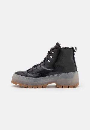 Botas negras de caña alta con acabado brillante, ribete de piel sintética en la parte superior, suela de goma transparente y suela exterior con dibujo texturizado para mayor tracción.