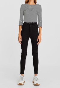 Jeans ajustados negros de cintura alta con bolsillos, combinados con una camiseta de manga larga ajustada blanca y negra a rayas y zapatillas deportivas blancas.