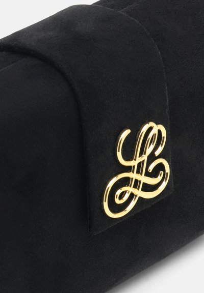 Sort ruskindshåndtaske hjørne med guldfarvet hardware på klap med sammenflettede initialer logo.