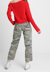 Rode cropped trui met ribbelstructuur; gecombineerd met licht camouflage cargobroek; model draagt witte canvas sneakers met een zwarte zool.