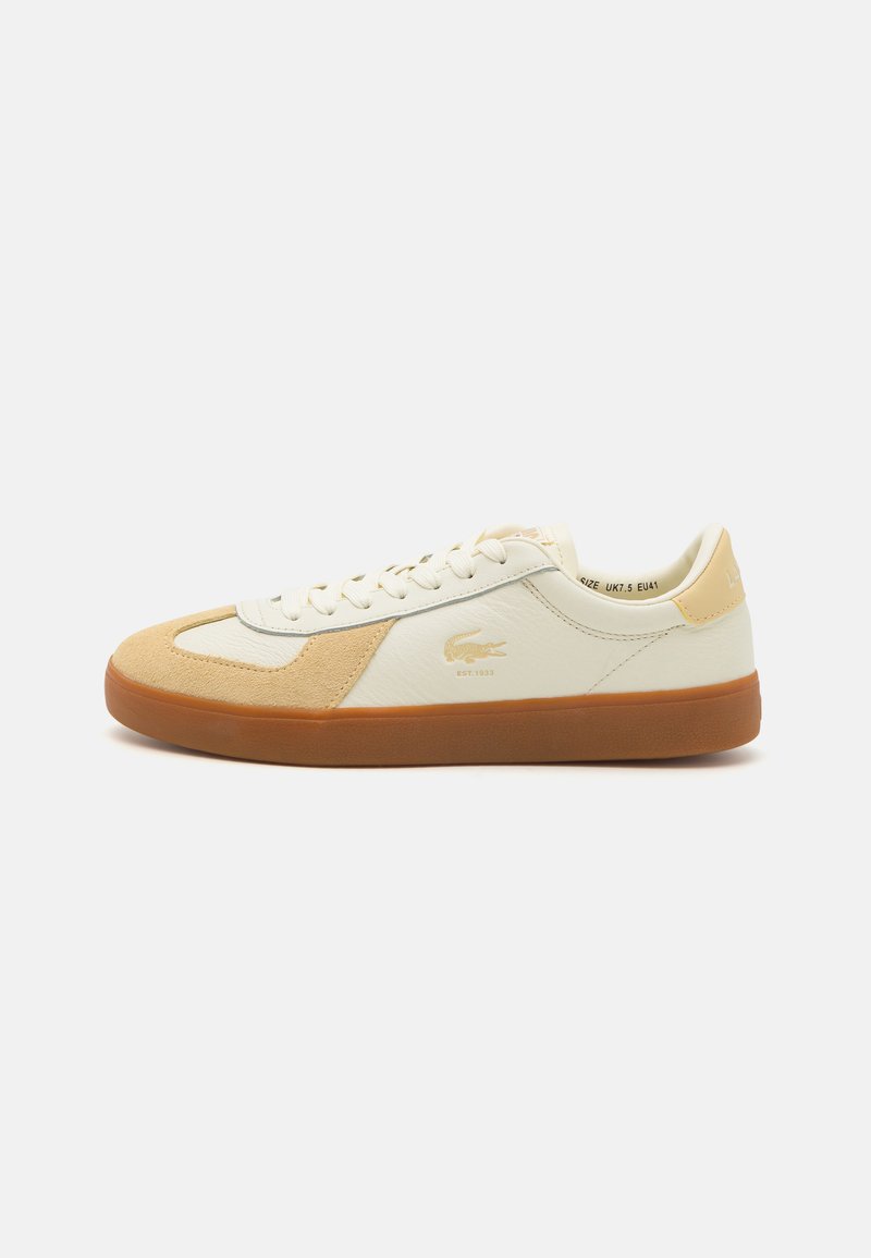 Zapatillas blancas y beige con parte superior de ante y cuero, puntera redonda, diseño con cordones, suela de goma y logo de Lacoste en el lateral.