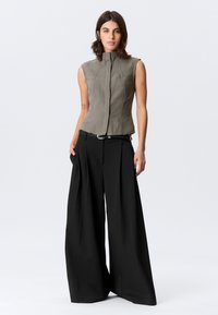 Haut sans manches, ajusté, en tissu vert olive texturé avec col montant. Associé à un pantalon noir taille haute, jambes larges.