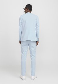 Svetlo modra obleka s slim-fit dizajnom, ki ima enojni razporek na jakni in usklajene hlače, v kombinaciji z belimi športnimi copati.