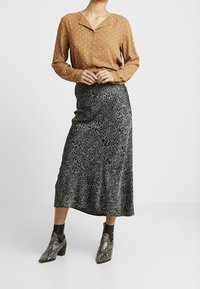 Blusa marrone a pois con colletto, abbinata a una gonna midi verde con stampa leopardata. Stivaletti alla caviglia in stampa serpente nera e argento.