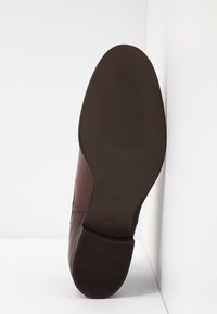Zapato de cuero marrón con una suela texturizada. El zapato cuenta con un tacón bajo y un logo grabado, destacando la durabilidad y la comodidad.