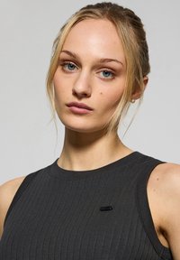 Top senza maniche nero a coste con scollo alto, caratterizzato da un piccolo badge sul lato sinistro. Texture liscia e design aderente.