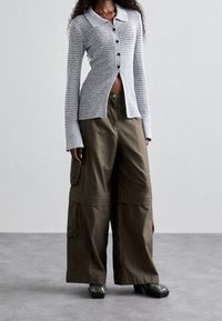 Cardigan lavorato a maglia grigio chiaro con colletto, chiusura con bottoni e maniche ampie, abbinato a pantaloni cargo verde oliva con tasche laterali.