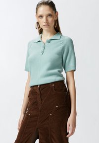 Svijetloplava pletena polo majica s kratkim rukavima, koja ima ovratnik i zatvaranje na gumb, u kombinaciji s smeškim korduroy suknjom s patentnim zatvaračem.