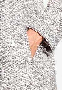 Grijze en witte geweven stof met een textuur en patroon. Close-up van een pocket geïntegreerd in een jas met een brede manchet.