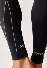 Zwarte compressiekousen met een aansluitend ontwerp, voorzien van contrasterende witte stiksels en de tekst "SNOCKS" op de manchetten. Zachte textuur.