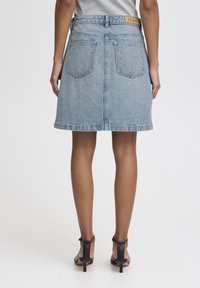 Denim A-line skirt, light blue, medium wash, with two back pockets and a visible brand label at the waistband. Flat hem and textured fabric.