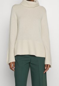 Beige polokrage tröja med ribbade ärmslut och nederkant, bärs med mörkgröna högmidjade byxor.