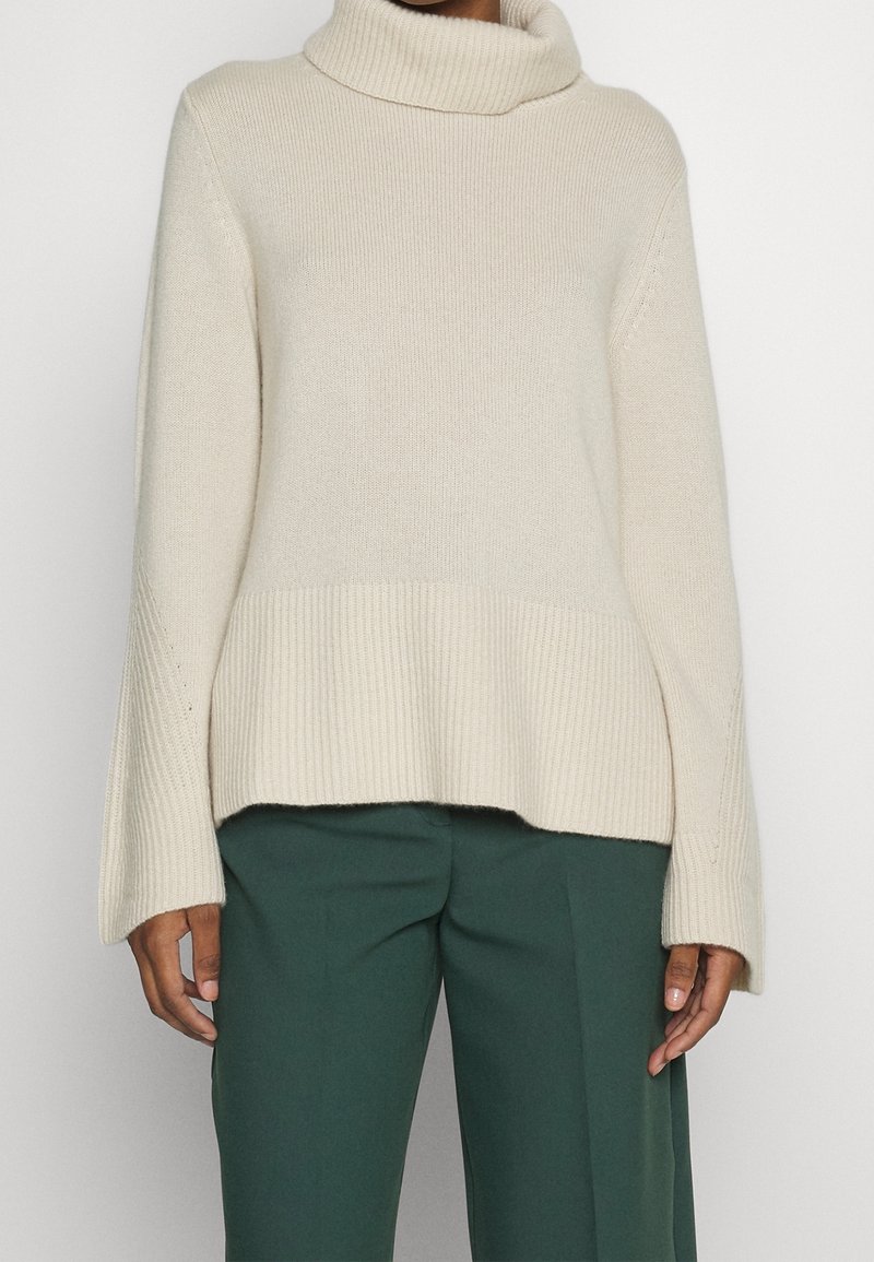 Beige polokrage tröja med ribbade ärmslut och nederkant, bärs med mörkgröna högmidjade byxor.