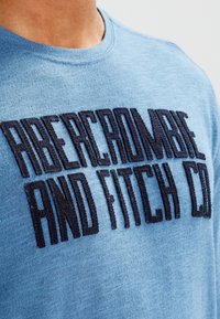Blauwe ronde hals sweater met donker geborduurde tekst "ABERCROMBIE AND FITCH CO." Zachte, gestructureerde stof met een casual pasvorm.