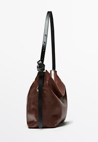 Borsa a spalla in pelle marrone con tracolla nera regolabile, chiusura a zip e finitura morbida e testurizzata. Presenta una forma arrotondata.