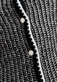 Svart och vit mönstrad cardigan med strukturerad stickning, kontrastkant och silverknappar som detaljerar framstängningen.