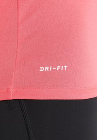Short-sleeve, coral Dri-FIT athletic shirt with smooth texture; features white Dri-FIT logo near the hem. Paired with black leggings.