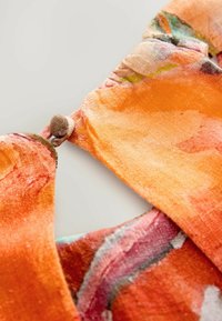 Blommönstrad tyg i orange och rosa nyanser, med en mjuk textur och en rund knappstängning vid halsen.