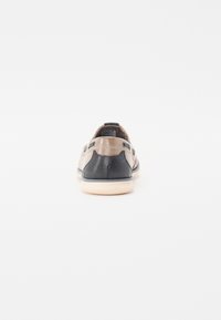 Lædersneakers i beige og marineblå, med en tekstureret overflade, lav profil og en let gummisål. Bagfra fremhæves syningsdetaljer.