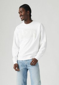 Sudadera blanca con el logo "LEVI'S" en bordado claro, cuello redondo, puños y dobladillo de canalé, combinada con jeans de color azul claro.