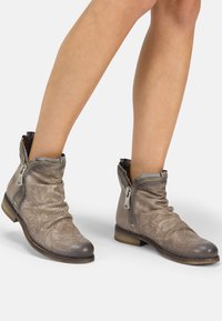 Bottes chevilles en cuir gris clair avec texture perforée, fermetures éclair latérales, design décontracté et petit talon en bois pour une stabilité accrue.