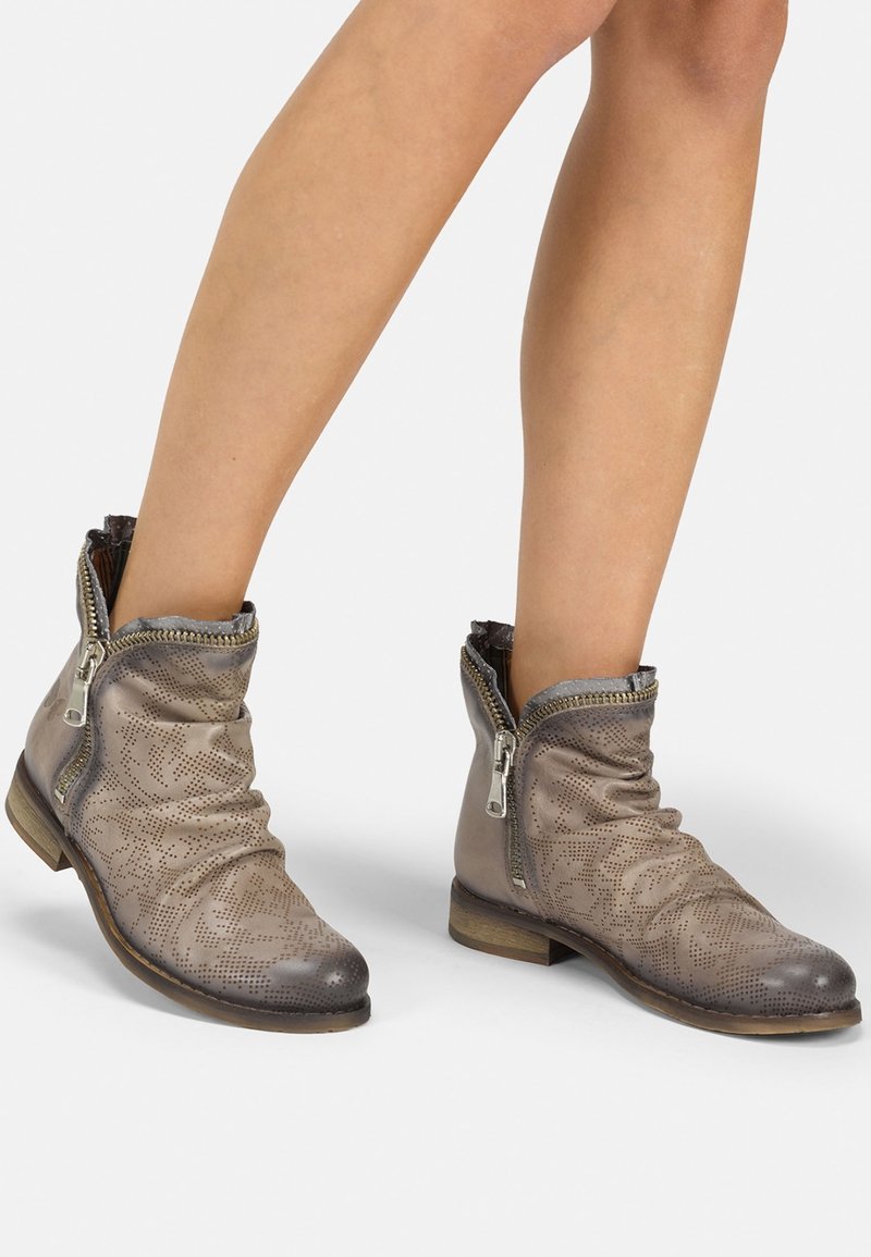 Bottes chevilles en cuir gris clair avec texture perforée, fermetures éclair latérales, design décontracté et petit talon en bois pour une stabilité accrue.