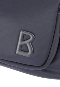 Szara torba kurierska z teksturowaną powierzchnią, klapką zamykającą i wyraźnym, wypukłym akcentem w postaci litery "B" na przodzie.