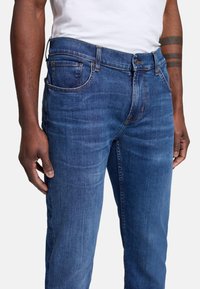 Jeans i mörkblå denim med en mjuk yta, femficksdesign och knappgylf. Anmärkningsvärd sömnad på fickorna.