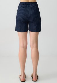 Pantaloni corti blu navy con texture a coste, vita elastica e taglio dritto. L'orlo cade appena sopra il ginocchio, con tasche laterali.