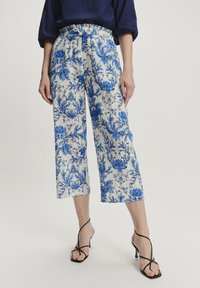 Culottes mit floralen Mustern in Creme mit blauen Designs. Mit einem elastischen Bund und verkürzter Länge. Getragen mit schwarzen, hohen Sandalen.