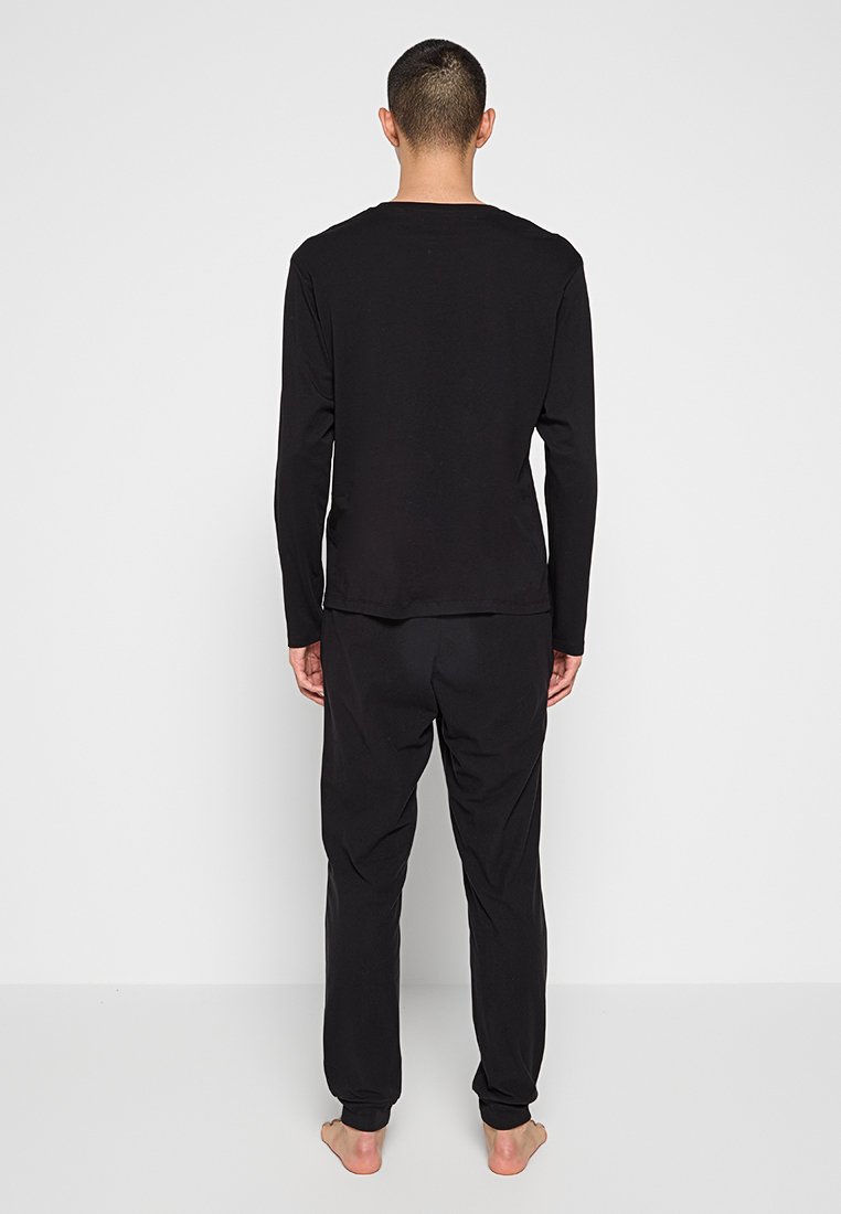 Top negro de manga larga combinado con pantalones negros a juego, ambos hechos de una tela suave. El diseño es simple, sin patrones ni acentos visibles.